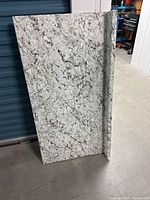 Granite countertop piece leaning against storage door, showing speckled white and gray pattern and attached backsplash.