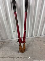 Bolt cutters with long red handles, black rubber grips, and a rusty cutting head. Photo shows wear and rust consistent with heavy use, confirming seller's description.