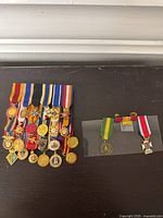 Set of 18 medals arranged in two rows with multi-colored ribbons and various designs including stars, crosses, and seals, displayed on a dark surface