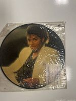 Front side of the Michael Jackson picture disc vinyl record showing Michael Jackson in a white jacket, enclosed in original plastic sleeve with minor creasing.