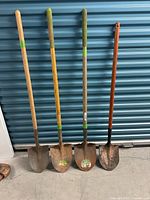 Four garden shovels standing upright, displaying wooden handles and metal blades with visible rust and wear.