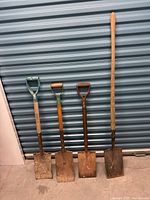 Four square shovels arranged side by side showing varying handle types and used metal blades with rust and dirt.