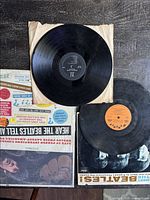 Top view showing three vinyl records with partial protective sleeves and album covers. Vinyls have surface wear; covers have edge and ring wear.