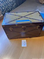 Photo of closed antique child's steamer trunk showing brown exterior with metal rivets in X pattern and three metal clasps on front