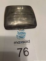 Closed antique sterling silver rectangular case with horizontally lined texture and slight tarnish, placed on a MaxSold Clutter Relief Services card with lot number 76 visible.