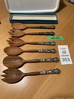 Full view of six salad utensils in two designs showing wooden tops and sterling silver handles.