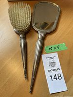 Full view of sterling silver brush and mirror set on wooden surface, showing the polished silver handles and the bristles of the brush.