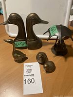 Overview of all six brass bird figurines including bookends, umbrella duck, quails and long-neck duck on a wooden surface.