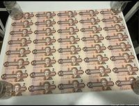 Full view of uncut sheet displaying 8 columns by 5 rows of intact two-dollar bills on white surface held at corners by jars