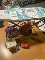 Ironing board with blue Mickey Mouse cartoon characters, visible table surface and other items, two tins including a red tin in the background, piggy banks on the side