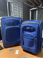 Two royal blue luggage pieces with telescoping handles and front pockets shown standing upright.