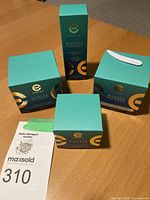 Four unopened Elizabeth Grant Modern Defense skincare products on a wood surface. Packaging shows turquoise color with gold accents.