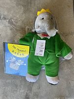 King Babar stuffed animal wearing green outfit and yellow crown, shown with The Travels of Babar book.