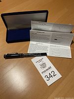 Pen displayed on table with case and pamphlet explaining refills and pen usage, lot tag shown