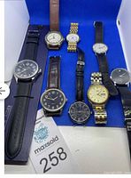 All 8 men's wristwatches displayed on a blue background showing different strap types and dial colors.