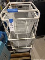 Full front view of three white metal mesh pull-out baskets arranged vertically on a white metal frame.