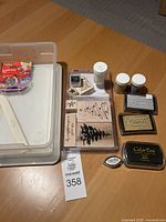 Top-down view of the storage container holding stamps, ink pads, embossing powder jars, and a white tool on wood floor.