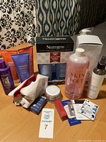Wide view showing full assortment of toiletries including boxed Neutrogena set, AVON hair products, Aussie shampoo, Skin Soft body wash, white cosmetic bag, and several small boxed items and samples.