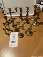 Wide view showing all 14 brass candlesticks of various shapes including koi fish pair, twisted 3-arm, horseshoe, and others.