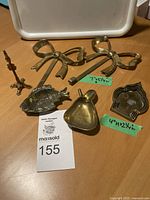 Vintage brass items arranged on wooden surface including pear dish, fish figurine, doll coat stand, bow hooks, and nesting man pieces.
