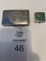 Photo showing the rectangular Richard Hudnut compact and smaller Celma rouge case side by side on a white surface with auction number card beneath.