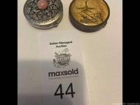 Photo showing two vintage makeup compacts on a white surface with auction tag below them