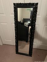 Full length black framed mirror resting against closed doors showing overall condition and design
