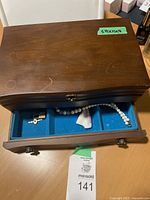 Wooden jewelry box showing top surface and part open drawer with vintage necklaces and a brooch inside.