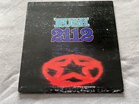 Front cover of Rush 2112 vinyl album, black background with red star emblem showing wear and edge scuffs.
