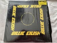 Front album cover with black background and yellow BILLIE EILISH text.