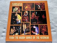Front cover of Nirvana's album 'From the Muddy Banks of the Wishkah' with multiple live shot photos of band members on orange background.