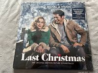 Front cover of the Last Christmas soundtrack album showing a man and woman seated on a bench in a snowy outdoor setting.