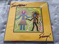 Front cover of Santana 'Shango' vinyl album sealed in shrink wrap showing yellow cover with colorful tribal figure artwork