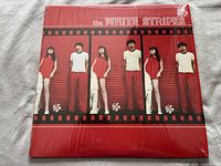 Front cover of the white vinyl album showing band members in red and white clothing with filmstrip design and band name.