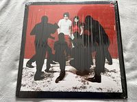 Front cover of The White Stripes White Blood Cells album, shrink wrapped with original artwork showing the band members against a red background with black silhouette photographers.