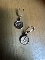 Photo showing both cherub earrings with circular pendant and red stone on lever back hooks from an angle.