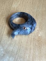 Ring carved in the shape of an elephant head with gold inlaid eyes, showing the trunk curled and eyes visible, iridescent gray stone material.