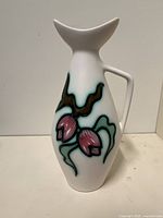 White ceramic pitcher with pink, black, and turquoise floral design, upright position showing full body and handle.