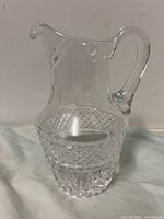 Front view of the clear cut crystal pitcher showing the diamond-cut pattern on the lower body and smooth upper body with handle and spout.
