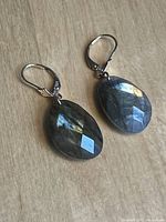 Pair of faceted labradorite earrings with visible iridescence on 14kt leverback clasps, photographed on a light green fabric background.