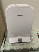 Front view of the white Homech humidifier with control knob and power cord visible on a cloth surface.