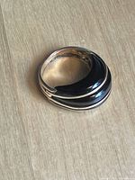 Top angled view of the black stone ring with gold-colored metal bands placed on wood surface.