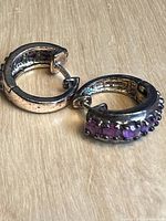 Close-up of earrings showing silvertone metal with purple stones and hinged clasp.