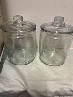 Two clear glass canisters with lids placed side by side, showing their shape and size.