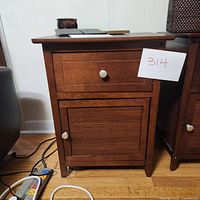 View of one dark wood night stand showing a single drawer and door with round knobs, on a hardwood floor.