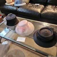 Three women's hats on glass coffee table with black sofa in background.