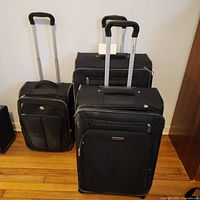 Three black softside suitcases with telescoping handles, two Samsonite and one American Tourister.