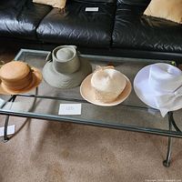 Four women's hats arranged on a glass coffee table showing all items in the lot