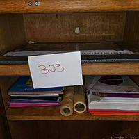 Shelf containing black construction paper pack, assorted colored sheets, two rolls of paper, and additional paper sheets.