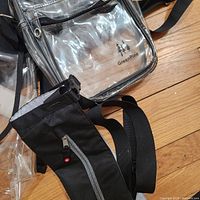 Closer view of the rectangular clear PVC bag with GreenPine logo and black crossbody strap alongside a black zippered pouch.